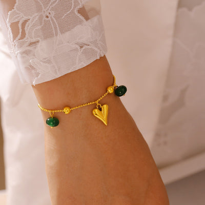 Gold heart charm bracelet with green beads worn on wrist