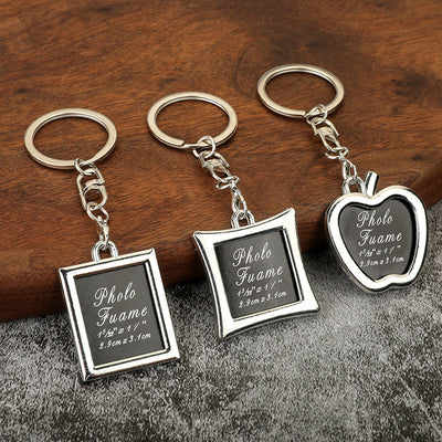 Three silver-tone photo frame keychains in rectangular, square, and apple shapes on a wooden surface.