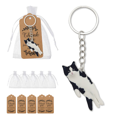 A black-and-white cat keychain is displayed beside a white drawstring bag and kraft thank-you tags.