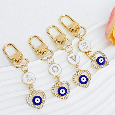 Four gold-tone keychains arranged to spell L-O-V-E, each with an enamel letter disc and a rhinestone heart evil eye char