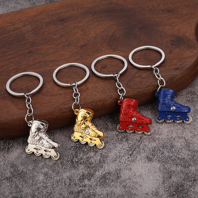 Four skate boot keychains in silver, gold, red, and blue rest on a wooden surface.