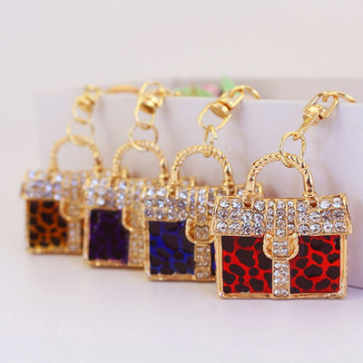Four handbag-shaped charms in red, blue, purple, and gold leopard prints are arranged in a row.