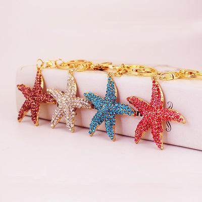 Four rhinestone starfish keychains in purple, white, blue, and pink are arranged in a row.