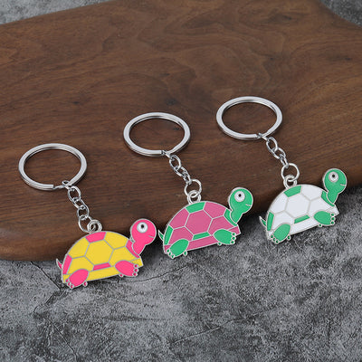 Three turtle keychains in pink and yellow, green and pink, and green and white rest beside a wooden surface.