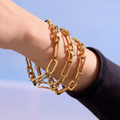 Stack of gold geometric paperclip link bracelets on wrist outdoors