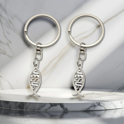 Two silver-tone keychains with openwork JESUS fish pendants on a marble surface.