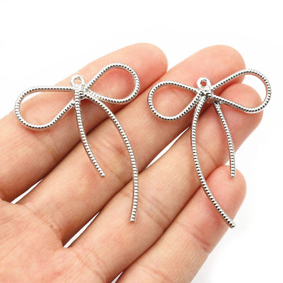 Image 1 showing silver tone long-tail bow charm with textured outline in the pictured colors and forms