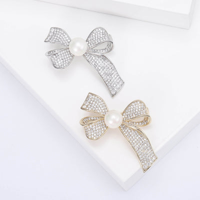 Grouped view of crystal ribbon bow brooch centered with a white pearl-like bead arranged together.