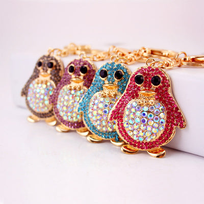 Four rhinestone penguin keychains in gray, purple, blue, and pink arranged in a row.