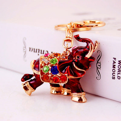 Red elephant keychain with multicolor stones resting against a white book.