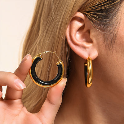Gold black oil drip thick hoop held beside matching worn earring