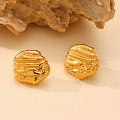 Pair of gold irregular ripple stud earrings beside natural stone