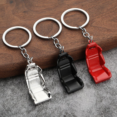Three car seat keychains in silver, black, and red rest on wood and gray fabric.