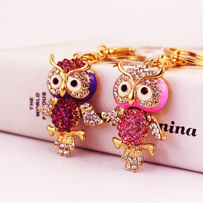 Two gold-tone owl keychains in purple and pink with faceted stone accents.