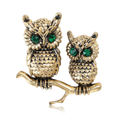 Two textured owls with green eyes perched on a branch shown on a white background.