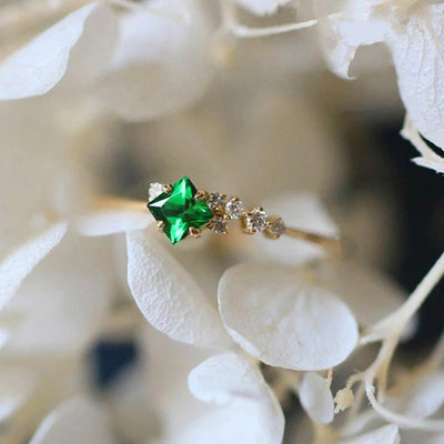 Gold green princess cut ring on white hydrangea petals