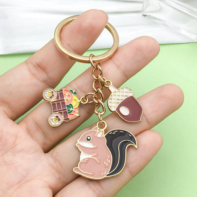 A gold-tone squirrel keychain rests on a hand with acorn and harvest cart charms.