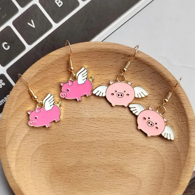 Two pairs of pink winged pig enamel earrings side and face styles on wood dish