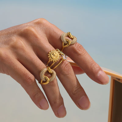 Hand wearing gold interlocking pave link rings stacked with other gold rings