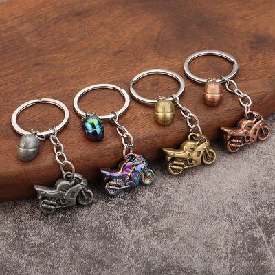 Four motorcycle keychains in silver, multicolor, gold, and copper finishes displayed on wood.
