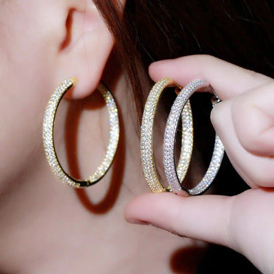 Large clear-stone oval hoop earrings beside an ear