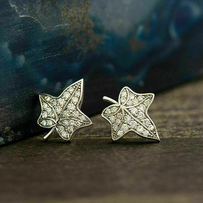 Silver pavé maple leaf studs on dark wood with blue slate backdrop