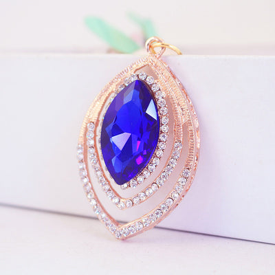 Angled front view of the feather pendant with a blue faceted center stone and clear rhinestones.