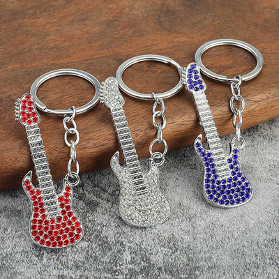 Three electric guitar keychains with red, clear, and blue rhinestones on a wooden surface.