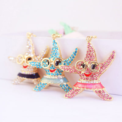Three gold-tone starfish charms with pink, blue and clear rhinestone finishes stand in a row.