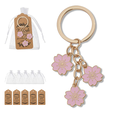 A pink three-flower keychain shown beside white drawstring bags and brown thank-you tags.