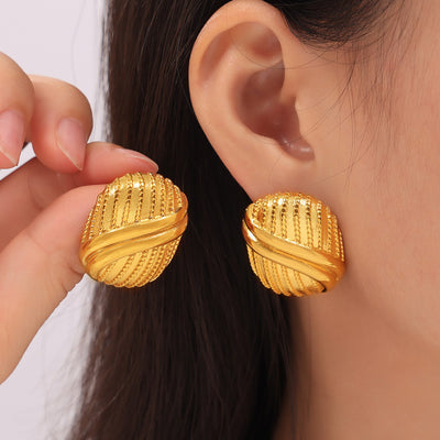 Model holding gold multi-line oval stud earring beside ear wearing pair