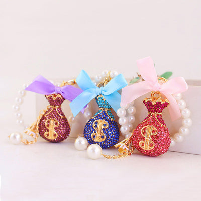 Pink, blue and purple rhinestone money bag keychains displayed together with matching ribbon bows.
