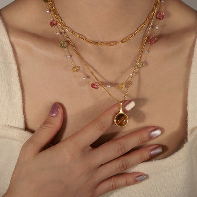 Model wearing gold tiger-eye teardrop pendant with layered necklaces