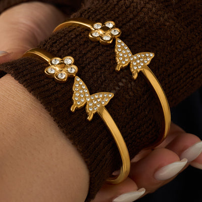 Two gold butterfly flower crystal bangles stacked on brown sleeve