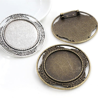 Round silver-tone cabochon brooch tray with layered borders and a pin back in a group view on a white background