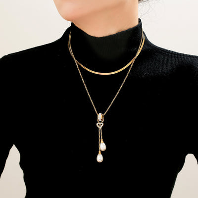 Model in black turtleneck wearing gold snake chain and pearl heart drop necklace layered