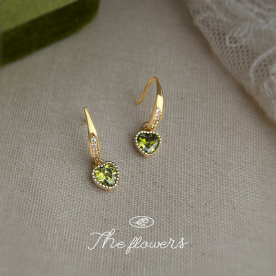 Gold-tone clear-stone bar and lime heart drop earrings on cream fabric.