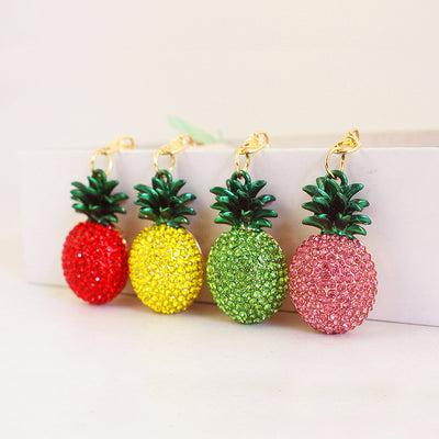Four pineapple keychains in red, yellow, green, and pink stand in a row.