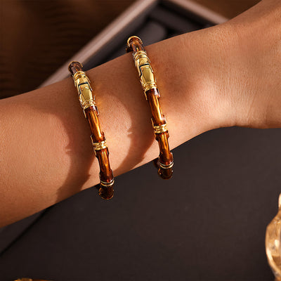 Two amber bamboo open cuffs with gold hardware stacked on wrist