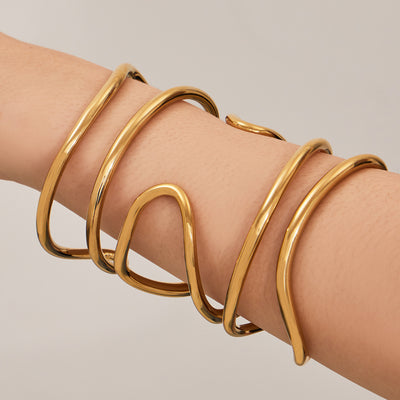 On-wrist view of sculptural crossing loop open cuffs in main image 1.