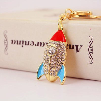 Close-up of a gold-tone rocket charm with clear stones, a red nose, and blue fins