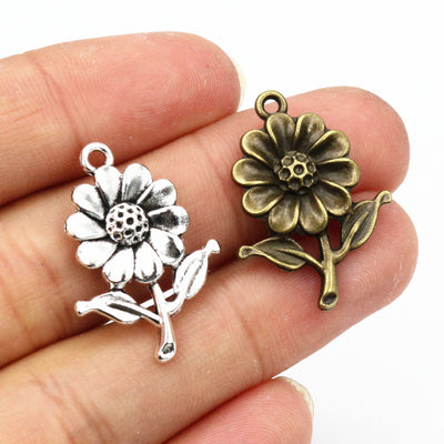 Overview of sculpted sunflower charms with layered petals, textured centers and short stems arranged on a light backgrou