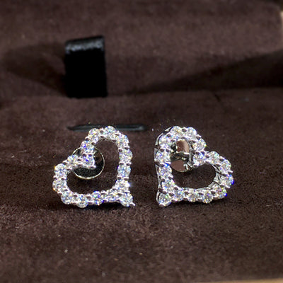 Pair of silver open heart clear pave stud earrings on dark brown surface