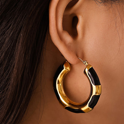 Gold black enamel hoop earring worn on ear close-up
