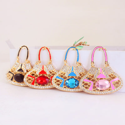 Four handbag-shaped charms in black, red, blue, and pink arranged side by side.