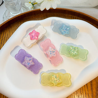 Six glitter star wave bar hair clips in mixed pastel colors on white tray