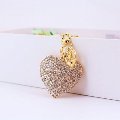 Clear stone-covered heart keychain hanging from the edge of a white box.