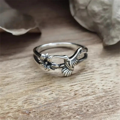 Antique silver hummingbird and flower dual band ring on wood surface