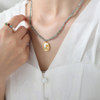 Model wearing blue green faceted bead necklace with gold rose oval pendant