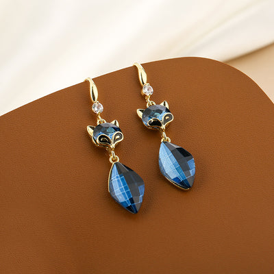Gold fox blue crystal drop earrings on brown leather surface angled view